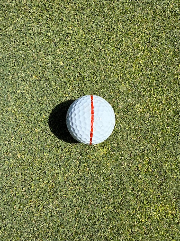A golf ball aligned with a red stripe on a sunlit green, perfect for sports themes.