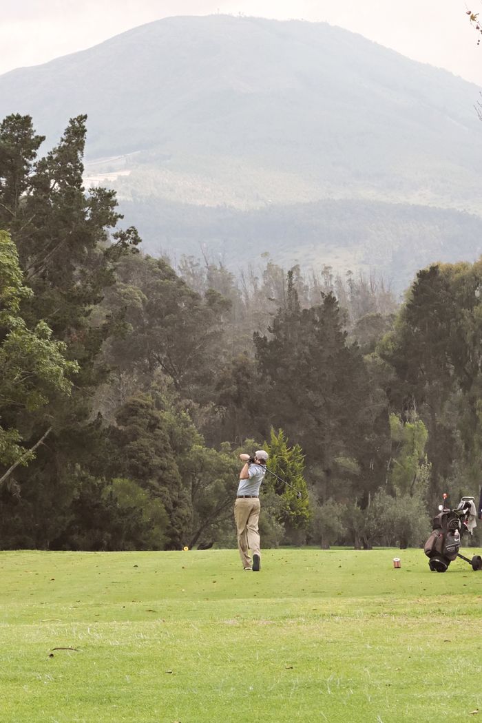 Golfer swinging on a lush green course under a mountain backdrop, perfect for outdoor sports themes.